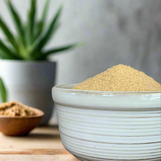 White bowl filled with brown sugar on a wooden surface with a blurred plant in the background